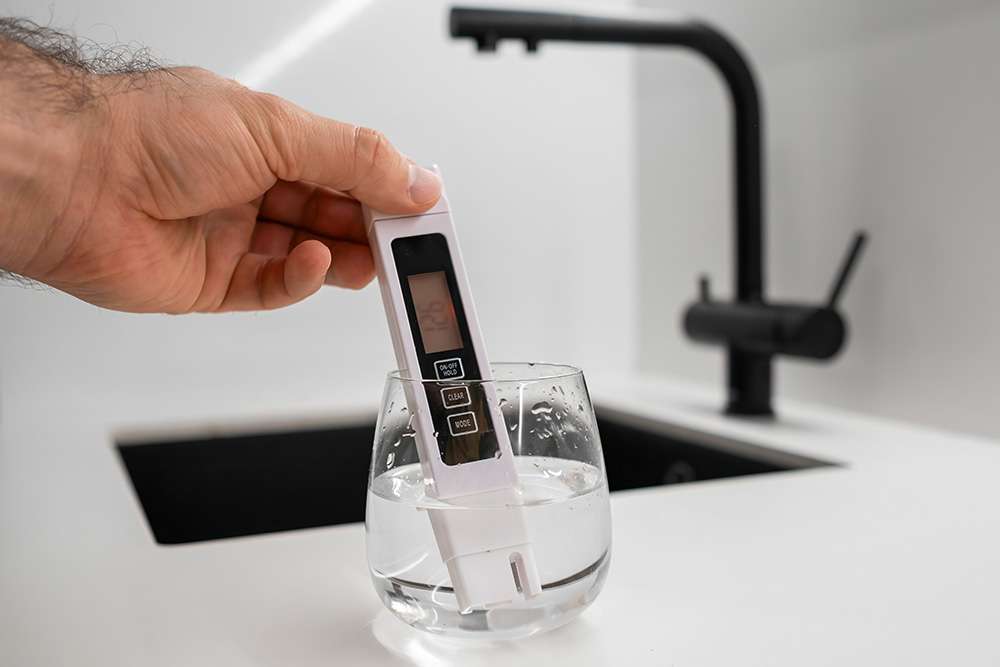 A man using a professional water testing device to test a glass of clear tap water