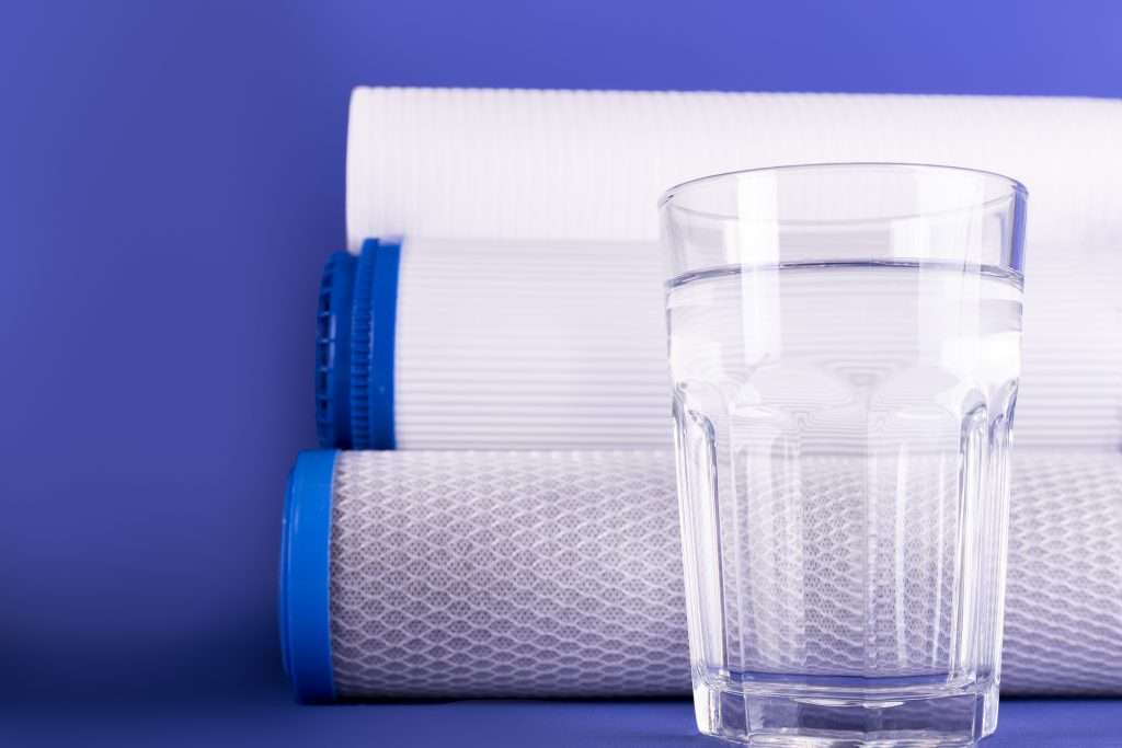 Set of three cartridges for water filter with clear glass of water isolated on violet background.